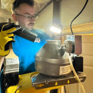 Technician performing booster fan cleaning on in-line dryer vent with gauge